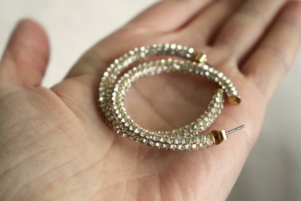 Close-up view of luxurious diamond-studded hoop earrings resting on a palm, showcasing gold and sparkling elegance.